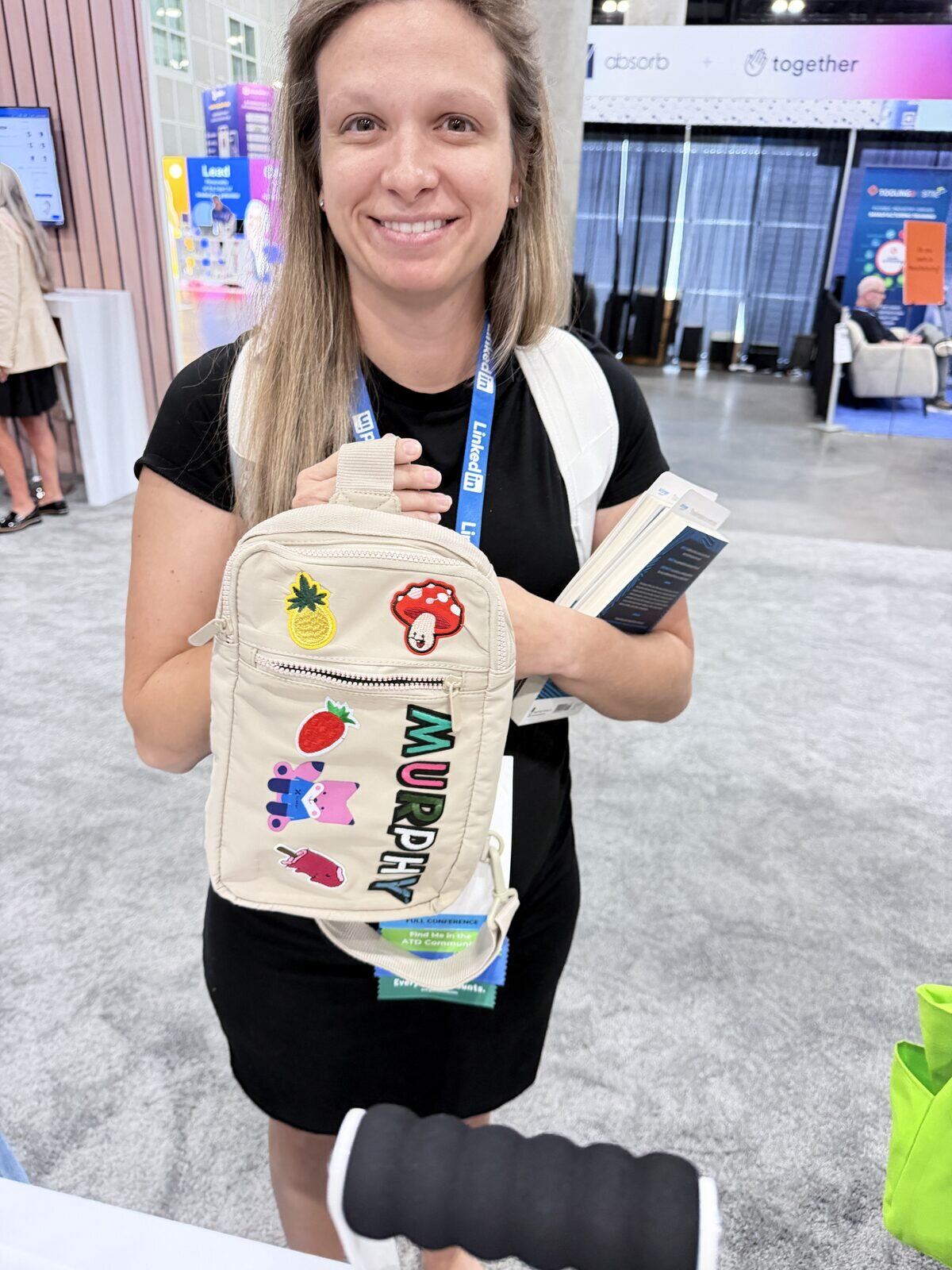 Smiling guest showing off a sling bag personalized with her name in pressed letters and fun patches